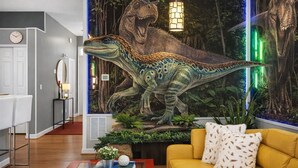 A living room with a sofa, a coffee table with books, a wall mural of a dinosaur, and a clock on the wall. - Animatronic Dinosaur Villa: 3 King Rooms, Theater & Private Pool Near Disney (Clermont)