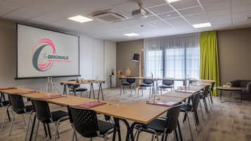 Una sala conferenze con un grande schermo che mostra un logo, diversi tavoli con sedie, un proiettore e una finestra con tende.