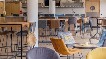 Un café moderne doté de plusieurs espaces de détente, comprenant des tables et des chaises, ainsi qu’un comptoir.