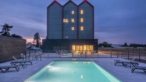 Een modern gebouw met een zwembad, ligbedden en terrasmeubels.