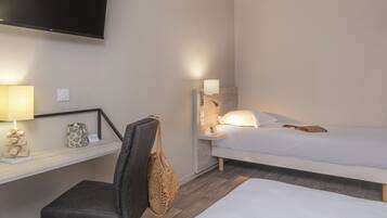 A hotel room with a bed, a desk with a lamp, a chair, and a wall-mounted TV.