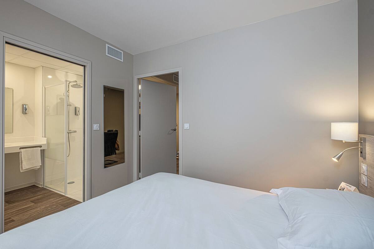Une chambre d’hôtel comprenant un lit, une salle de bain avec douche et une porte donnant sur une autre pièce.