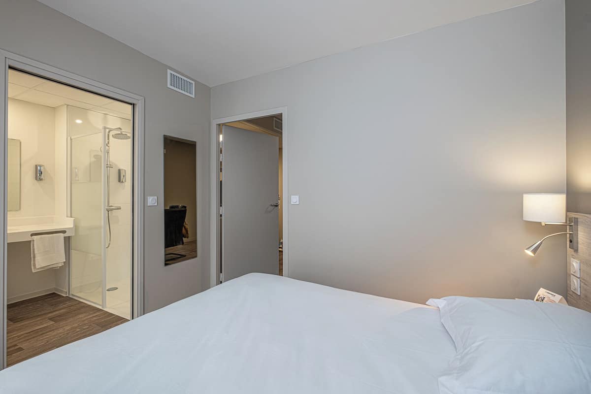 A hotel room with a bed, a bathroom with a shower, and a door leading to another room.