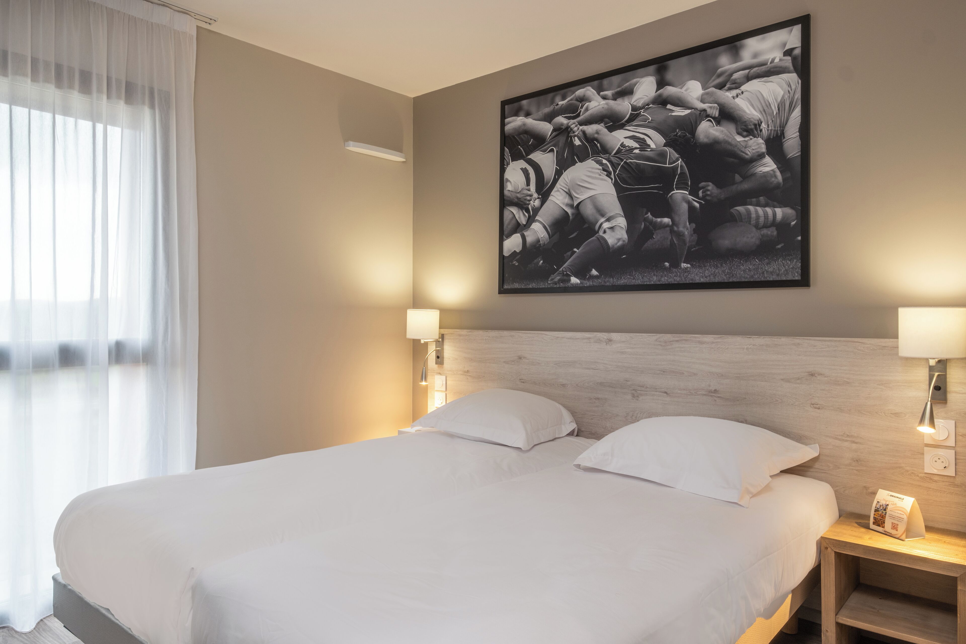 A hotel room with a large bed, two bedside lamps, a headboard, and a framed photograph on the wall.
