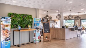 Een moderne receptiebalie met een houten toonbank, een groene wand met planten en een schoolbord.