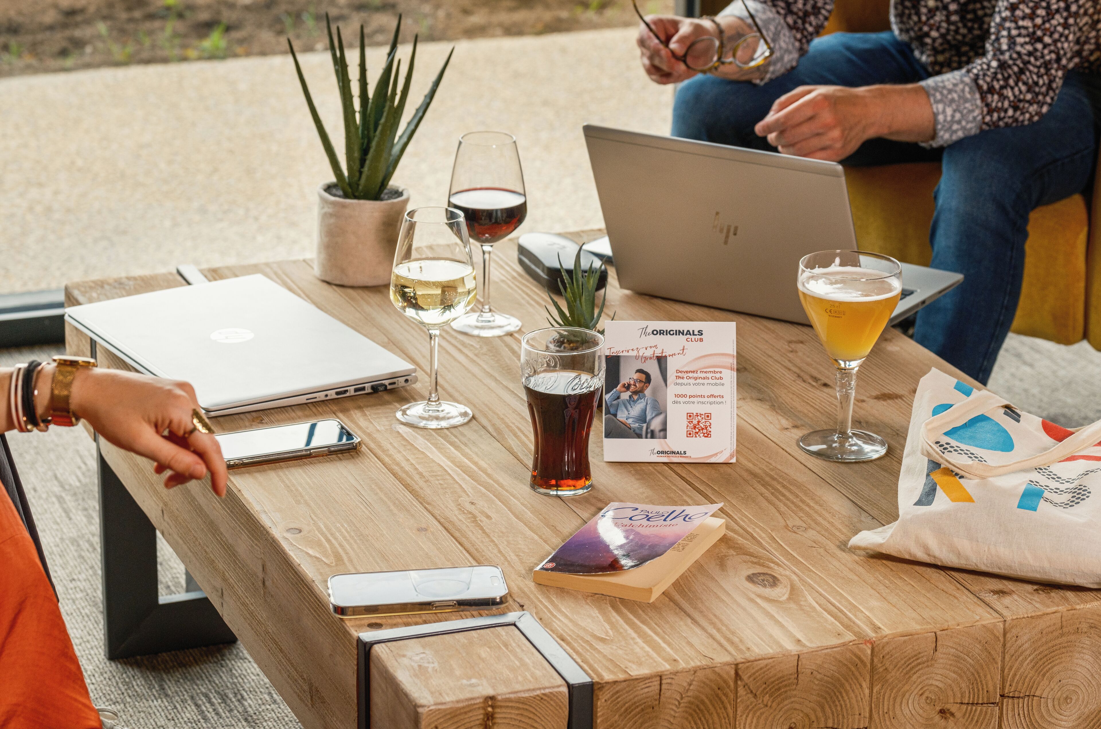 A wooden table with a laptop, wine glasses, a book, and a bag.
