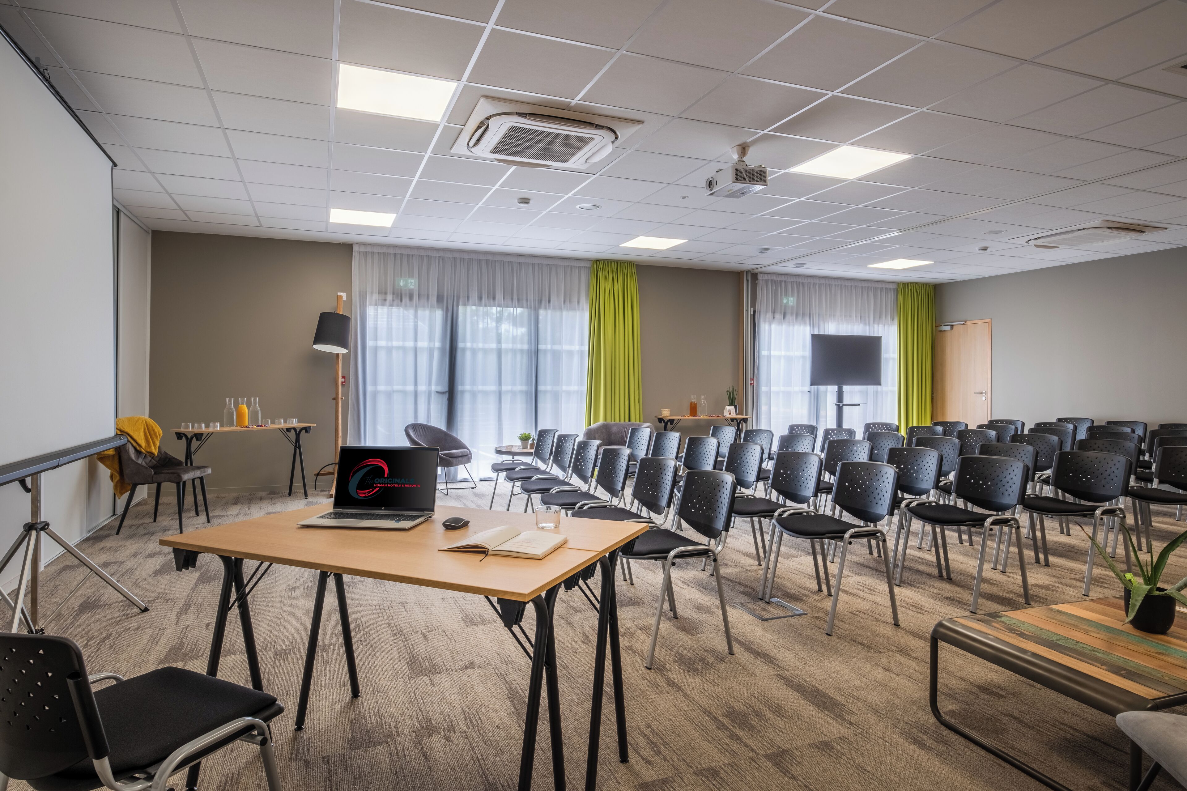 A conference room with a long table, multiple chairs, a projector screen, and a laptop on the table.