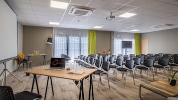 A conference room with a long table, multiple chairs, a projector screen, and a laptop on the table.