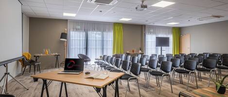 A conference room with a long table, multiple chairs, a projector screen, and a laptop on the table.