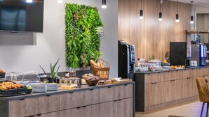 Een moderne ontbijtbalk met diverse etenswaren, een koffieapparaat en een aan de muur bevestigde televisie.
