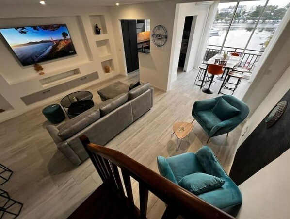 Un salon moderne avec un canapé gris, des fauteuils turquoise et un téléviseur fixé au mur.