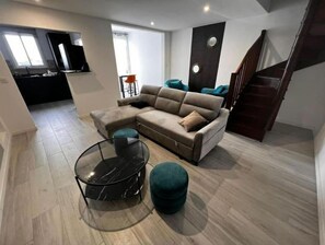 Un salon moderne avec un canapé d’angle, une table basse en verre et un pouf turquoise.