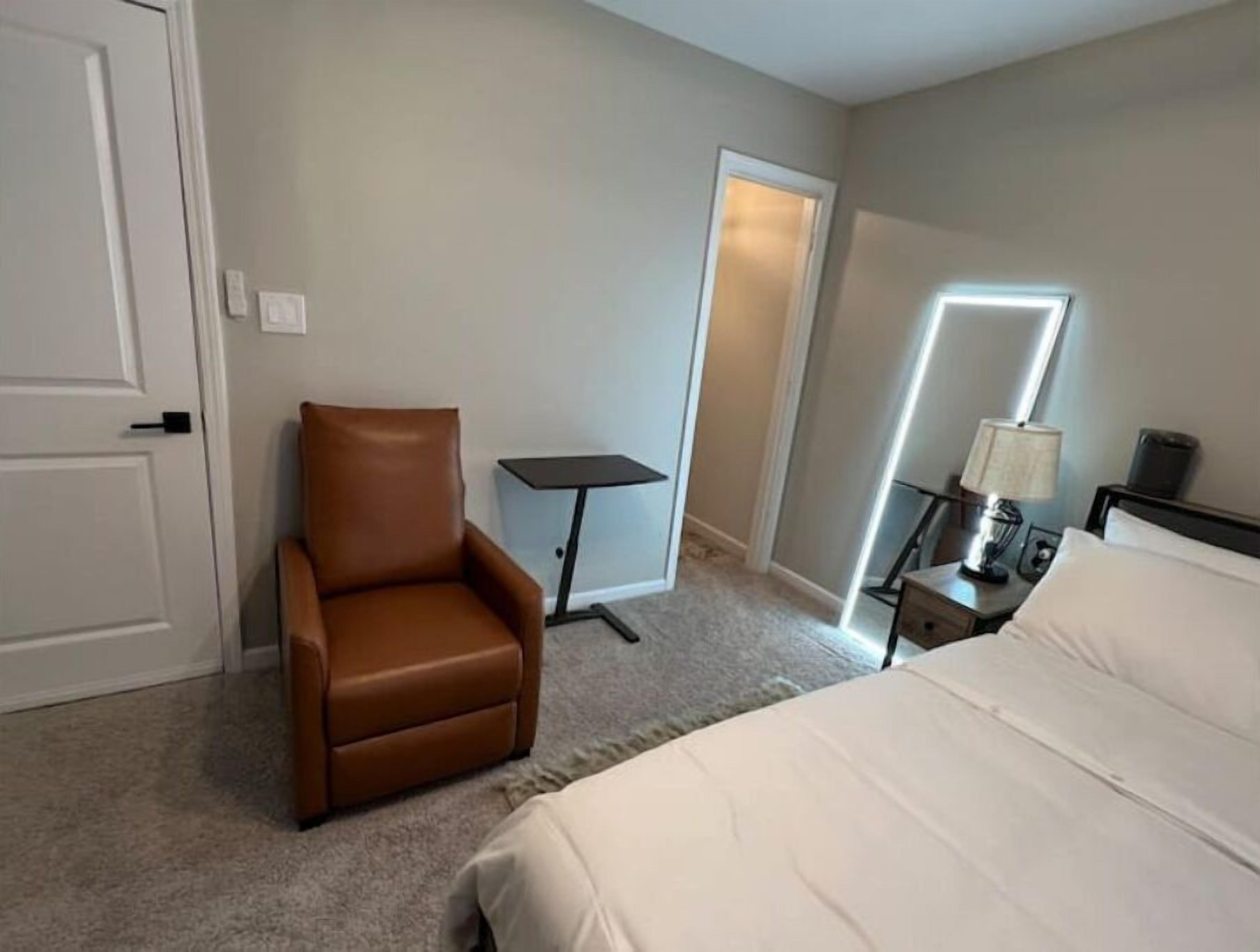 Ein Hotelzimmer mit einem Bett, einem braunen Ledersessel, einem kleinen Tisch und einem Nachttisch mit Lampe.