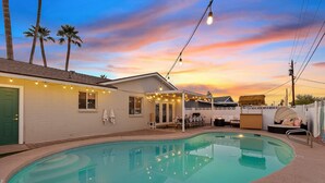 A swimming pool with a covered patio area, a green door, and string lights. - Heated Deep Diving Pool, Firepit, BeautyBar, Yard Games, 3 King + 2 Queen beds (Tempe)