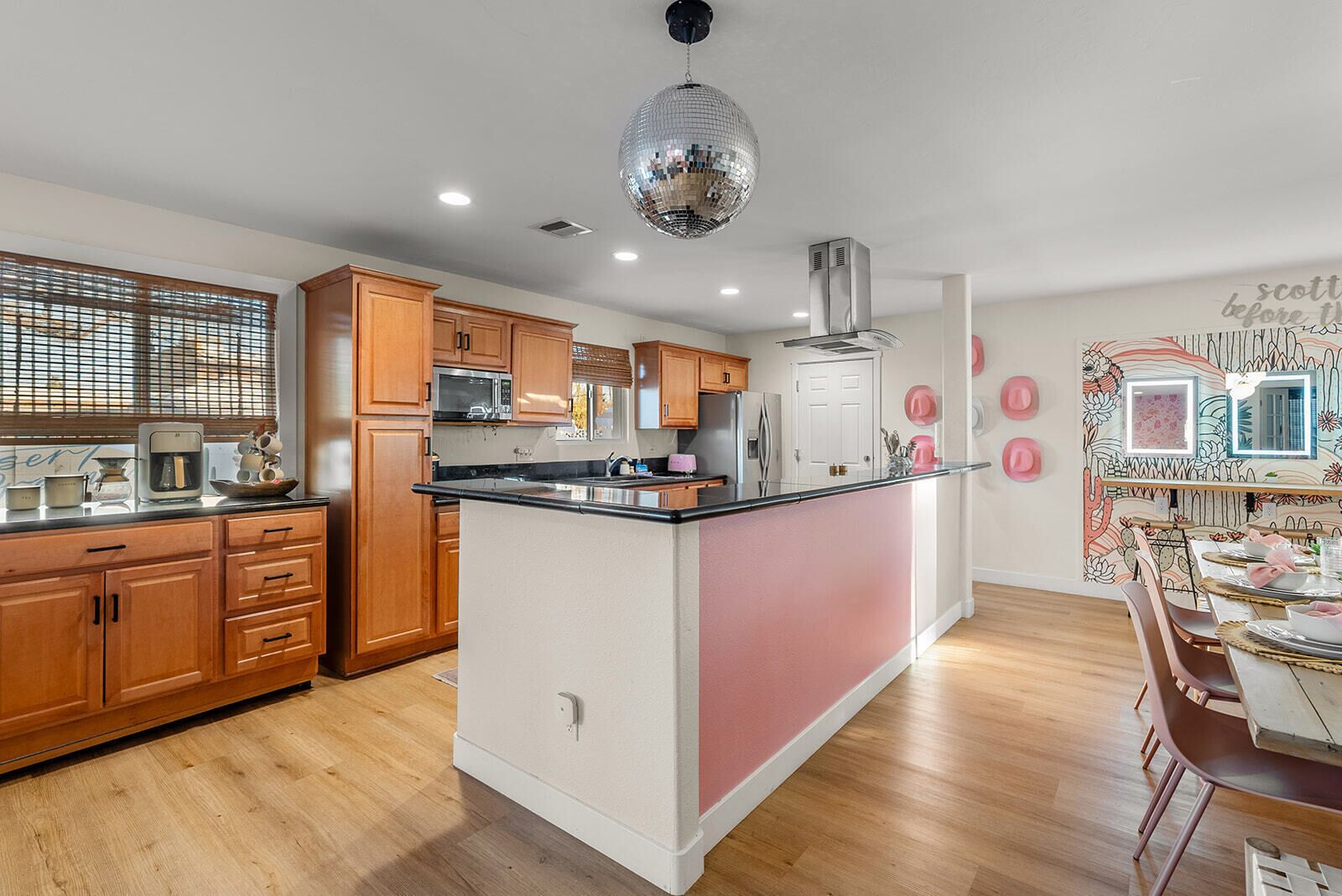 A modern kitchen with wooden cabinets, a central island, and a dining area with pink accents.