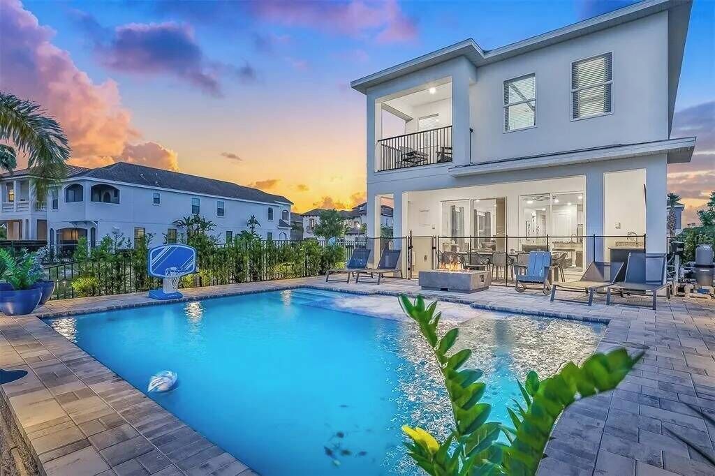 Une maison moderne à deux étages, dotée d’une piscine, de mobilier d’extérieur et offrant une vue sur le coucher de soleil.