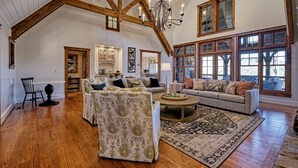 A spacious living room with high ceilings, wooden beams, and large windows.