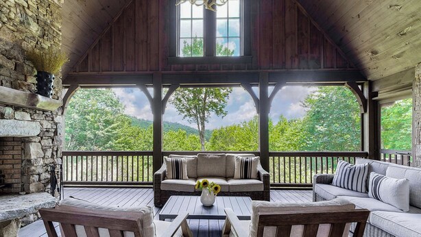 A covered porch with wicker furniture, a stone fireplace, and a view of green hills.