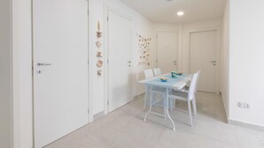 Et moderne, minimalistisk spiseområde med et hvidt bord og stole, en lys gulv og hvide vægge med dekorative skaller og et kunstværk.