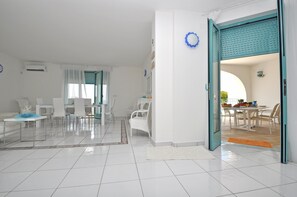 A bright, modern living room with a dining area, white furniture, and a teal door leading to another room. - Villa Esador by BarbarHouse (Torre Suda)