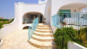 A white building with a stone staircase leading to a balcony with blue railings.