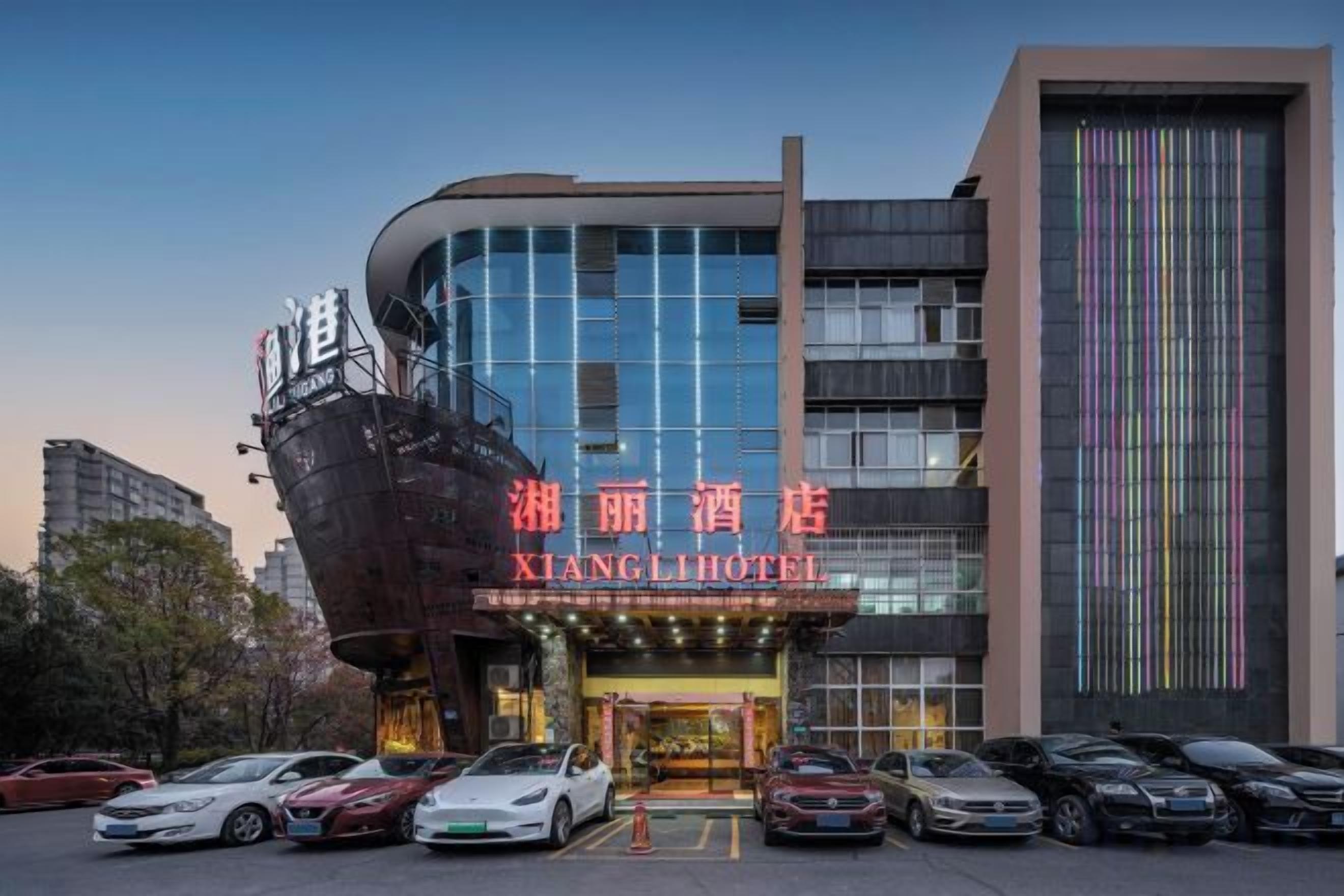 Un hotel con una facciata moderna, diversi piani e un parcheggio con diverse auto.