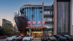 A hotel with a modern facade, a prominent sign, and a parking lot with several cars. - Xiangli Hotel (Shawan Park Subway Station, Changsha High Speed Railway South Station) (Changsha)