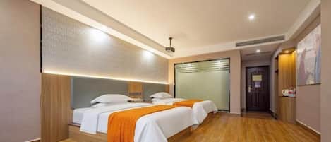 A hotel room with two beds, wooden flooring, a large mirror, and a door leading to another room.