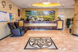 A hotel lobby with a reception desk, massage chairs, a decorative floor pattern, and a waterfall mural. - Xiangli Hotel (Shawan Park Subway Station, Changsha High Speed Railway South Station) (Changsha)