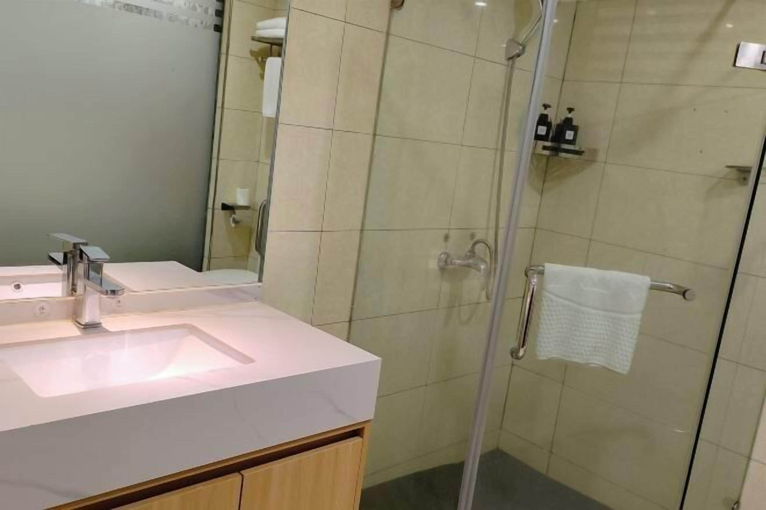 A modern bathroom with a white sink, mirror, and glass shower enclosure.