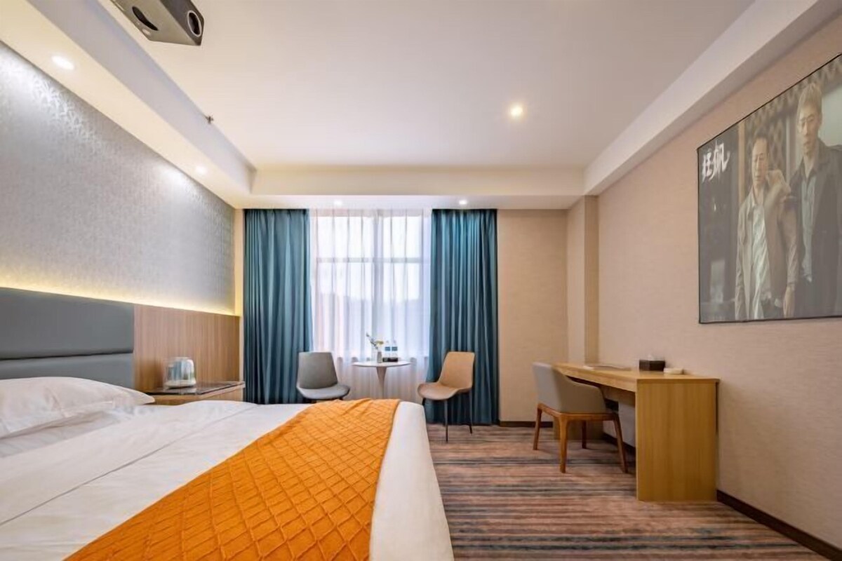 A hotel room with a bed, a desk, two chairs, a small table, and a large window with curtains.