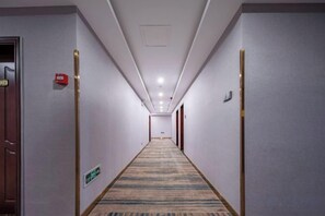A hotel hallway with carpeted floors, doors on both sides, and a fire alarm on the left wall. - Xiangli Hotel (Shawan Park Subway Station, Changsha High Speed Railway South Station) (Changsha)