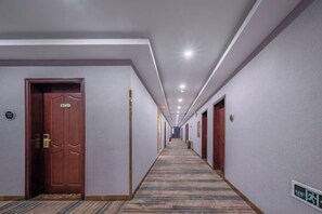 Corredor de hotel com portas em ambos os lados, piso coberto por carpete e iluminação no teto.
