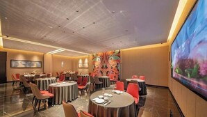 A modern dining area with round tables and red chairs, a large mural on the back wall, and a flat-screen TV on the right. - Xiangli Hotel (Shawan Park Subway Station, Changsha High Speed Railway South Station) (Changsha)