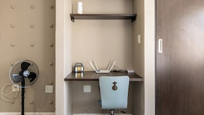 Una habitación con escritorio, silla, ventilador y puerta.