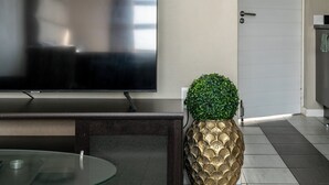 Una sala de estar moderna con un televisor de pantalla plana, una mesa de centro de vidrio y una maceta decorativa con forma de piña.