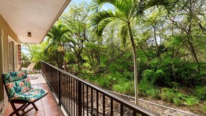 A balcony with a chair, a railing, and a view of dense greenery and a railway track.