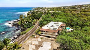A coastal building with a flat roof, a swimming pool, and a road adjacent to the ocean.