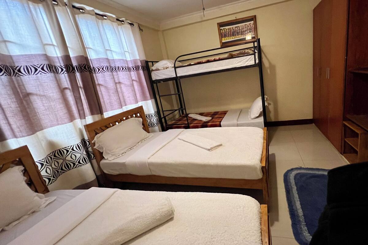 A room with two single beds, a bunk bed, a wooden wardrobe, and a curtain with a geometric pattern.