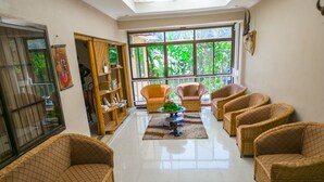 A spacious living room with wicker furniture, a coffee table, and a large window offering a view of greenery. - Runako Lodge (Arusha)
