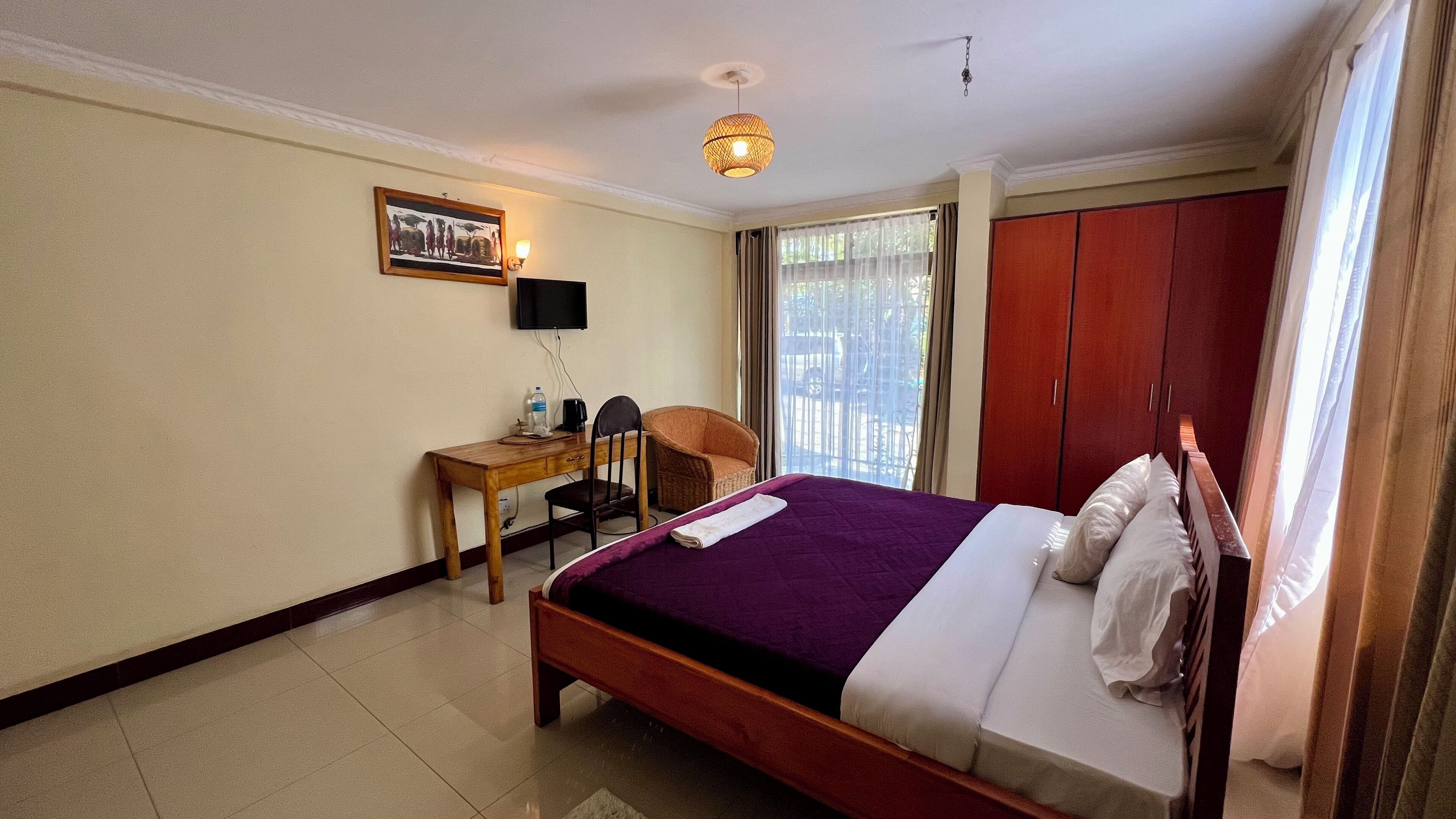 A hotel room with a bed, a desk with a chair, a television, and a wardrobe.