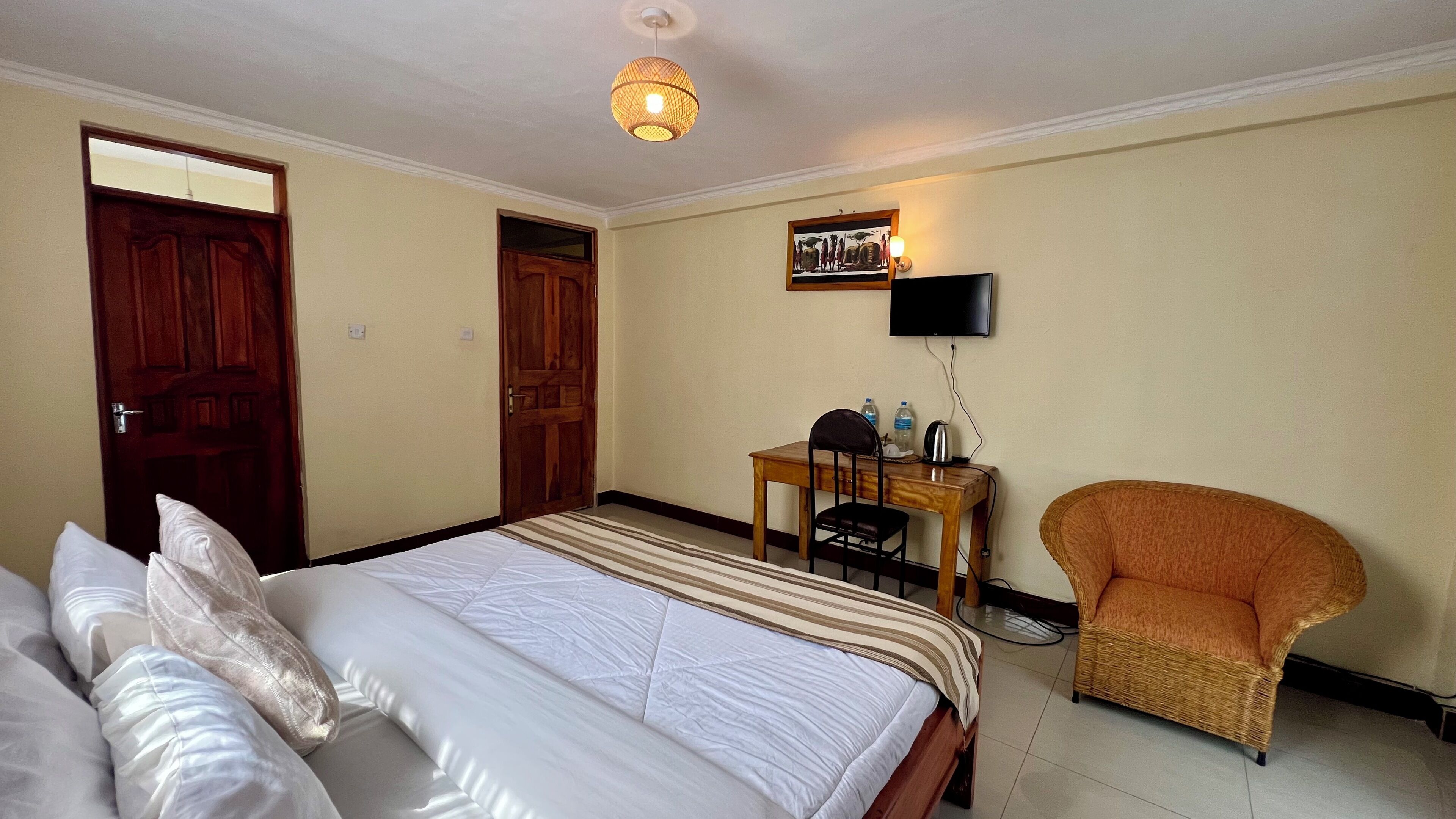 A hotel room with a bed, a desk with a chair, a television, and a wicker armchair.
