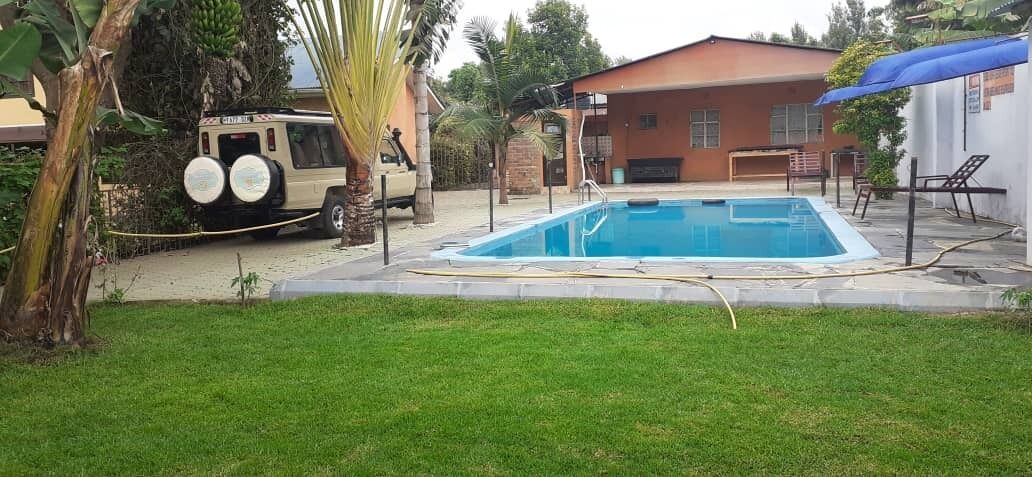 Una piscina con una fuente de agua azul, rodeada de un césped y un edificio con techo rojo.