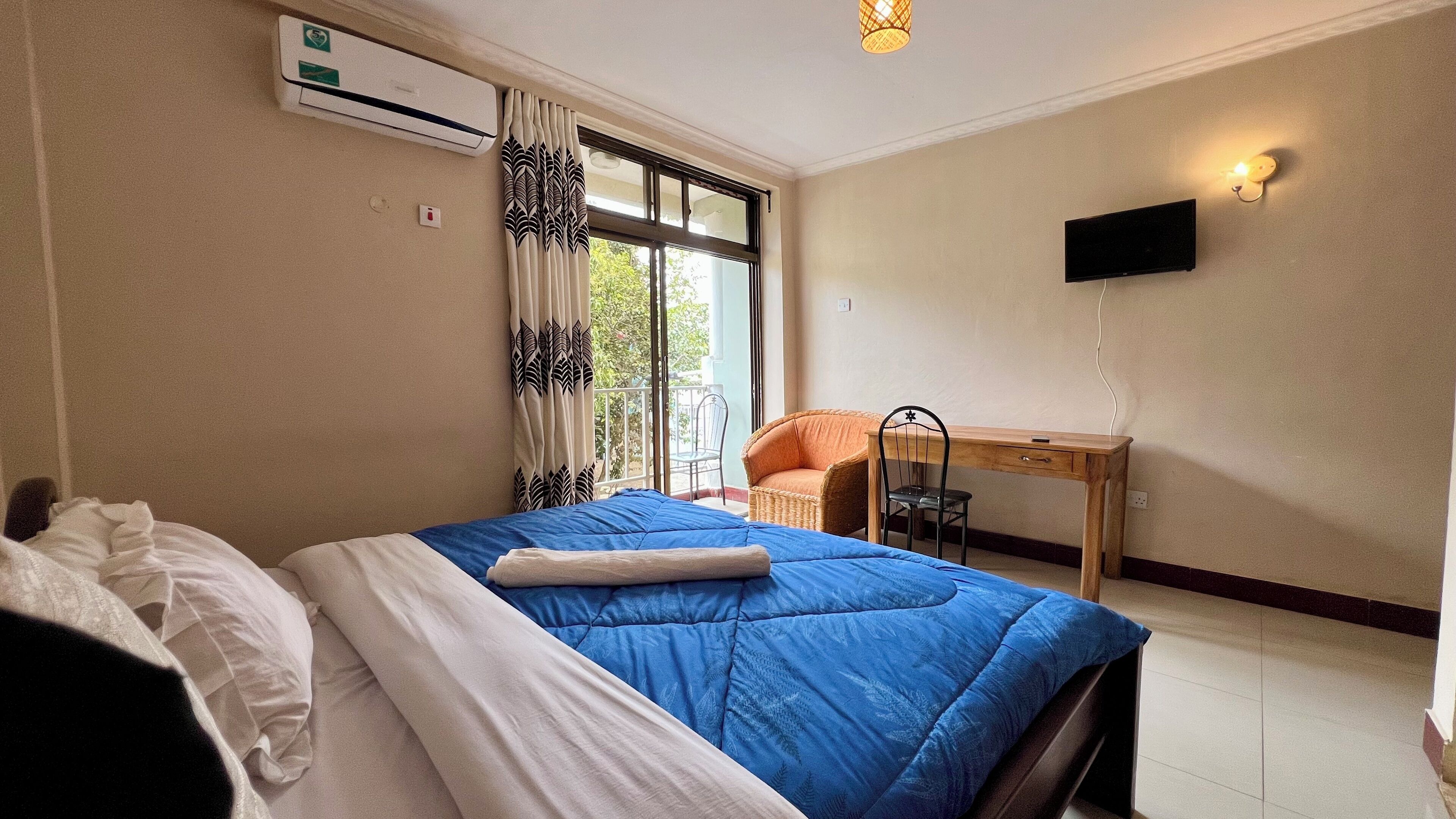 A hotel room with a bed, a desk, a chair, a TV, and a window with curtains.