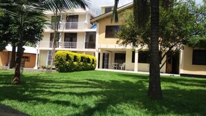 A multi-story building with balconies, a well-maintained lawn, and a neatly trimmed hedge. - Runako Lodge (Arusha)