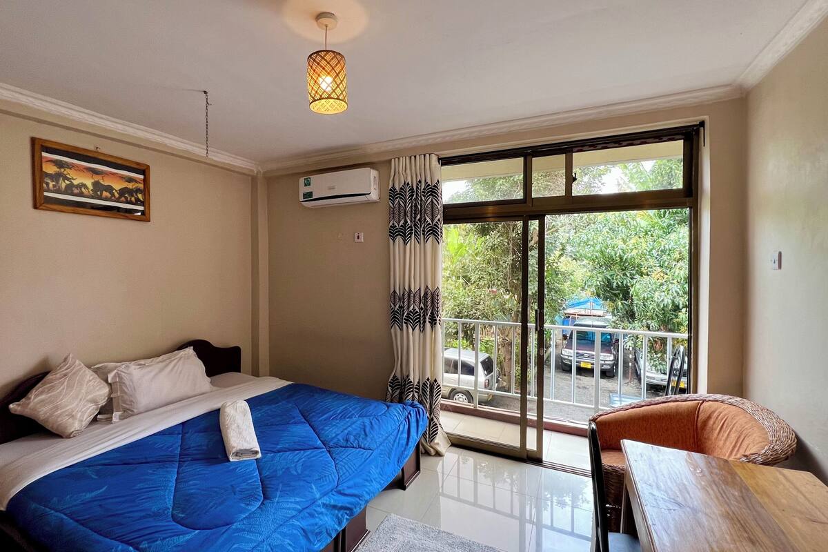 A bedroom with a bed, a nightstand, a chair, a window with curtains, and an air conditioning unit.