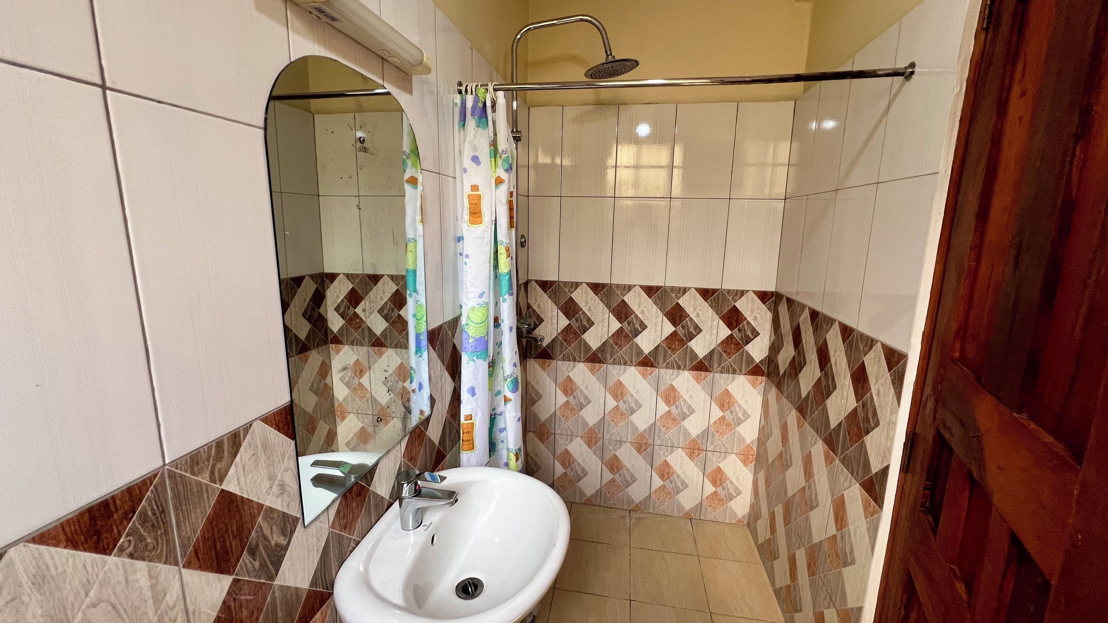 A bathroom with a white sink, a shower with a rain showerhead, and a mirror with a wooden frame.