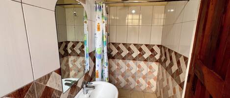 A bathroom with a white sink, a shower with a rain showerhead, and a mirror with a wooden frame.