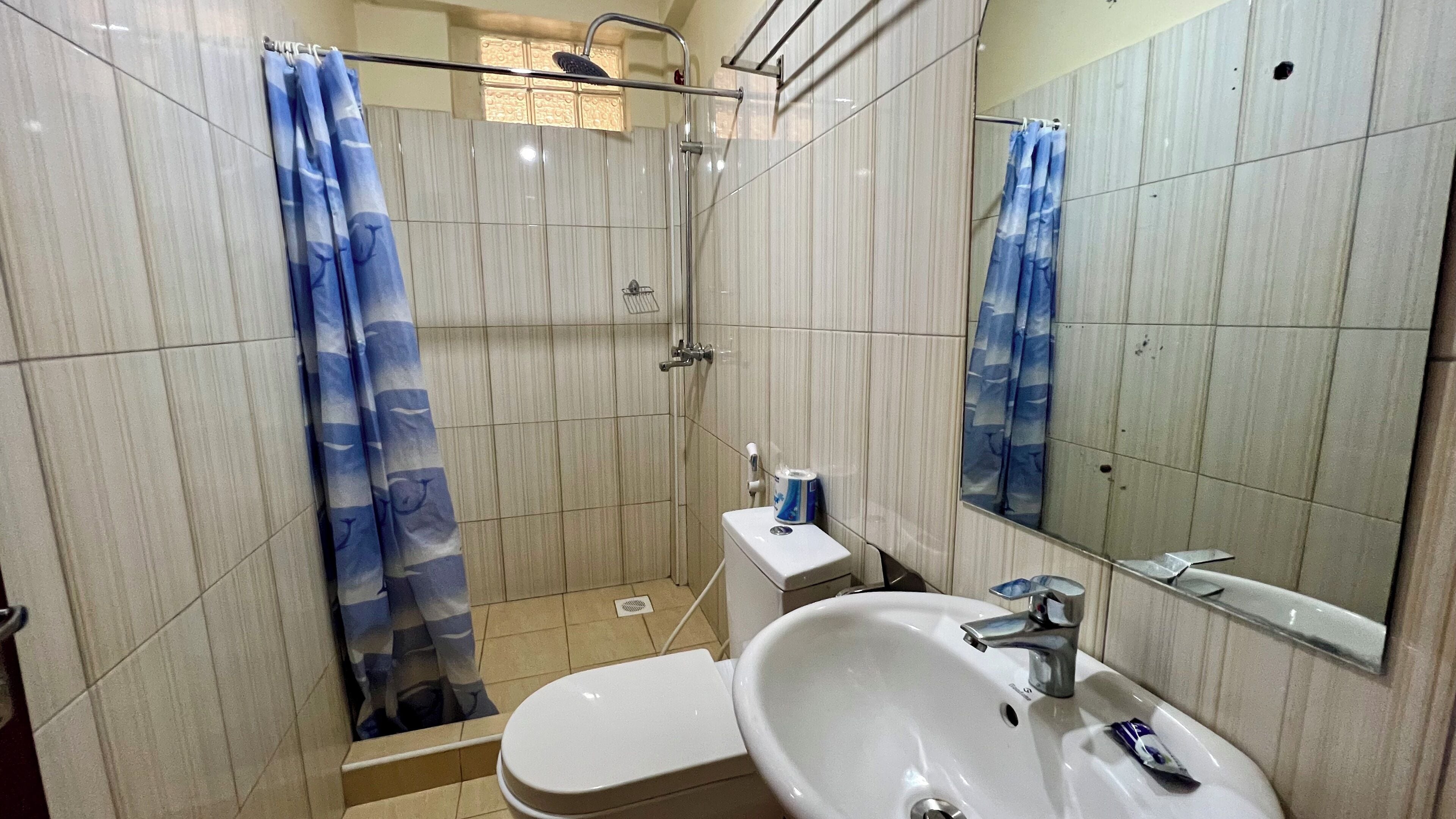Egy fürdőszoba zuhanyzóval, WC-vel, mosdókagylóval és tükörrel.