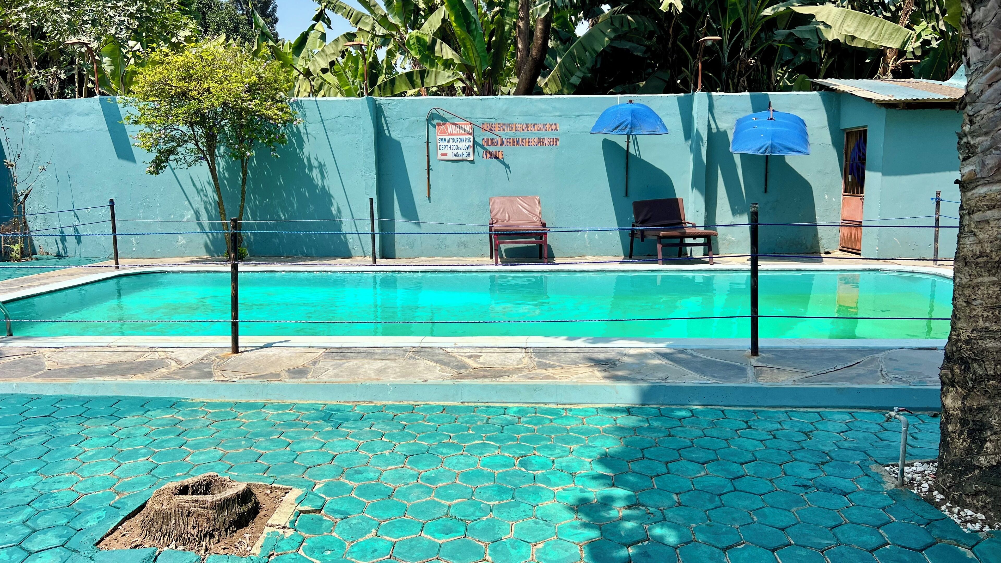 Una piscina con borde de azulejos azules, un cartel de seguridad y dos sombrillas.